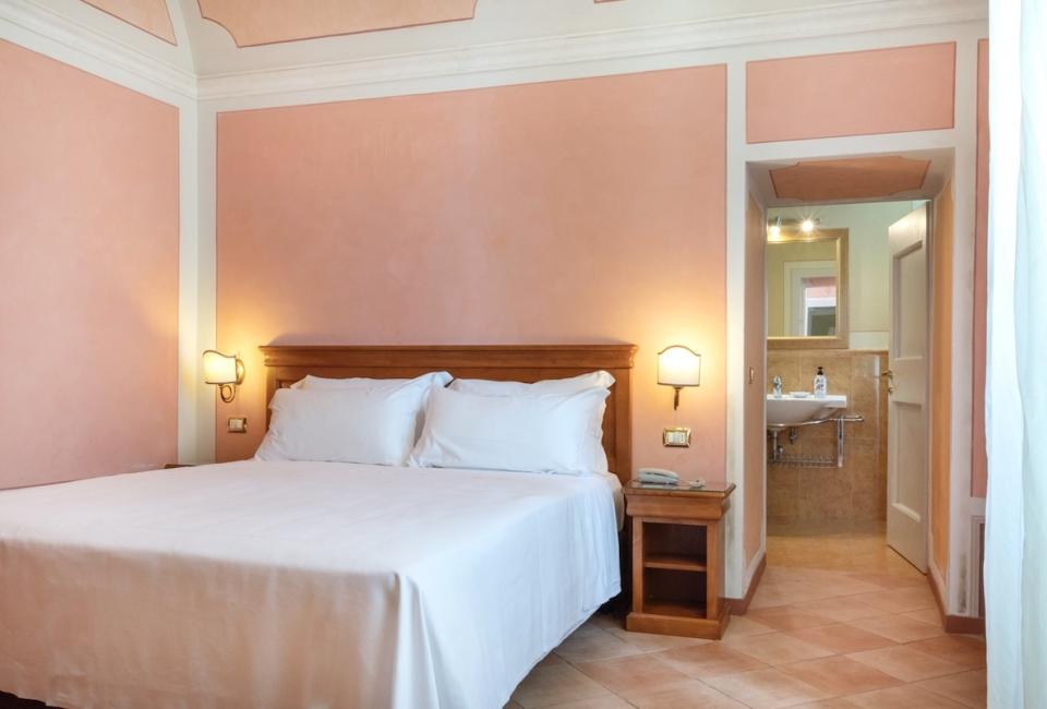 Bedroom with private bathroom, pink walls and wooden furniture.
